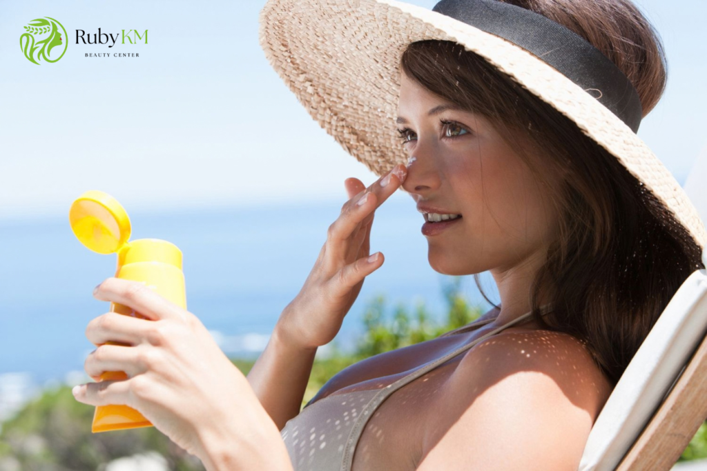 Woman applying sunscreen to her face outdoors while wearing a sun hat